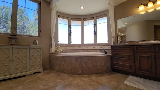 Luxurious curved bathtub in bright spa bathroom with tall windows