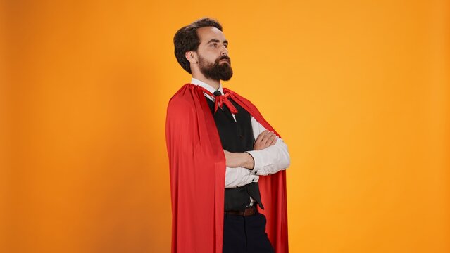 Powerful comic superhero with red cape standing against yellow background, feeling strong on camera. Dedicated valet superhuman with mantle working in restaurant dining industry.