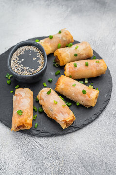 Crispy Egg rolls arranged on round slate plate with soy sauce and sesame seeds flat lay light background