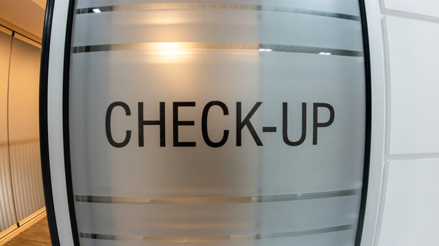 Close-up of a check-up text sign on a frosted glass door in a modern, clean medical clinic or hospital interior. Healthcare, wellness, and medical examination concept.