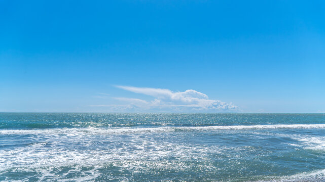 Wide sea horizon with blue water and white breaking waves under a clear sky with a large white cloud. Minimalist coastal landscape in Dalaman, Turkey.