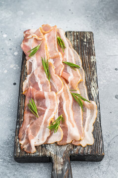 Cured pork belly, streaky bacon slices displayed on rustic wooden board with herbs perfect for stock images culinary design and menu concepts