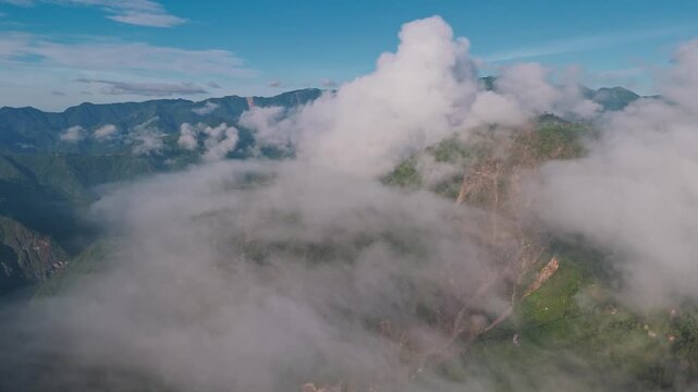 Clear mid-altitude drone view showing rugged Himalayan ridgelines with deeply incised valleys and canyon-like terrain. Cloud puffs at mid-level. Rocky cliff face and landslide erosion on the right 