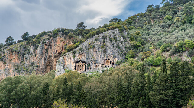 Ancient Lycian rock tombs carved into high cliffs surrounded by lush green trees in Dalyan, Turkey. Historic archaeological landmark and heritage scenery.