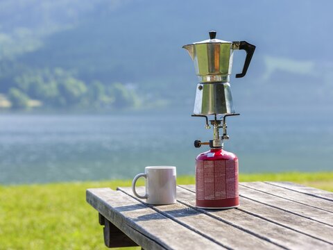 Espresso pot on a gas cooker next to a cup standing on a wooden table at the lake, Hallst&auml;tter See, Upper Austria, Austria