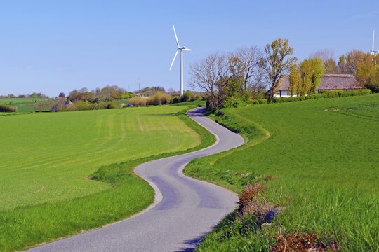 A winding road leads through green fields with wind turbines in the background, cycle tourism, manor house route, Norrebolle, Langeland, Denmark