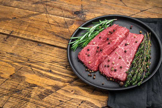 Raw marbled wagyu topside beef steaks with rosemary and thyme in iron pan. Gourmet red meat on wooden table top view.