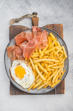 Spanish huevos rotos con jamon with fries and sunny egg yolk on ceramic plate overhead copy space