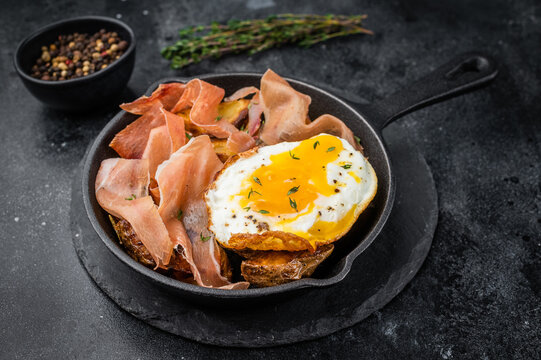 Huevos rotos Spanish comfort food with fried potatoes runny egg and jamon on dark stone background