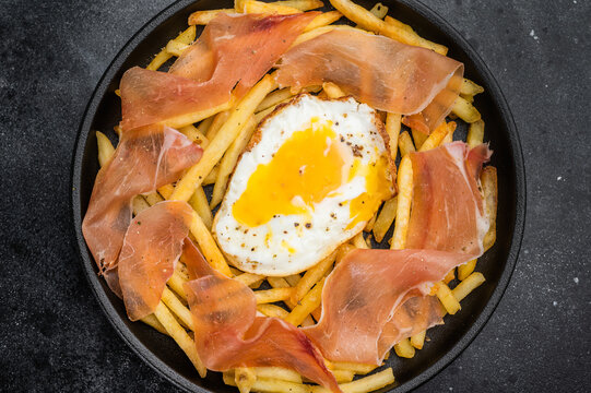 Spanish huevos rotos with broken eggs fries and jamon ham in black plate overhead copy space