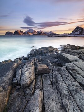 Rocky coast, snow-capped mountains in the background, Vestv&aring;g&oslash;ya, Lofoten, Norway