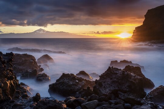 Sunrise on the beach at San Marcos. Rocks, sea and the sun. Tenerife and the Teide in the background. Long exposure. La Gomera, Canary Islands, Spain