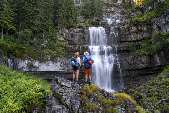 Young pretty hiker standing on rocks in front of Cascata di Mezzo waterfall, long exposure, Vallesinella, Brenta, Trentino, Italy