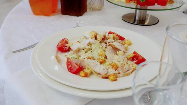 Gourmet caesar salad featuring grilled chicken, ripe tomatoes, crispy croutons on pristine white plate with refined dining arrangement