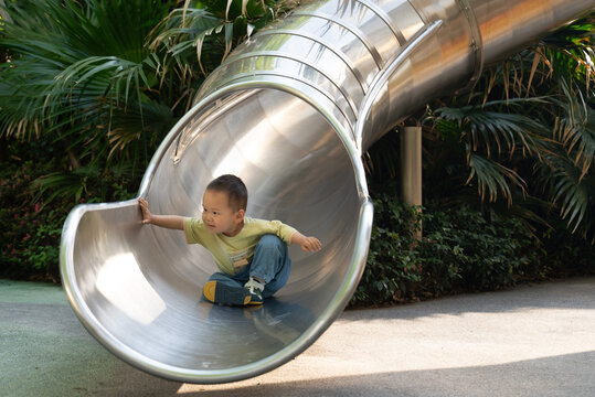 Asian toddler boy sitting at the end of metal slide