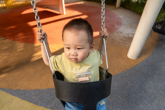 Toddler boy sitting in playground swing