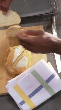 Vertical video: Holding serrated knife, cook's hands slicing round loaf in kitchen, checking crumb