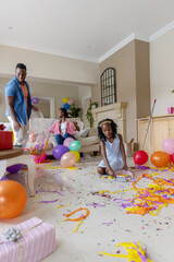 Obraz premium African American family tidying living room after party, child sweeping with dustpan, man with bag