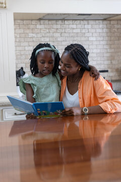 African American mother and daughter sitting in kitchen reading blue book child wearing green dress