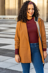 Adult woman standing in urban plaza wearing mustard-brown blazer and carrying shoulder bag © wavebreak3