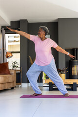Obraz premium Senior African American woman practicing standing yoga, balancing on purple mat in living room