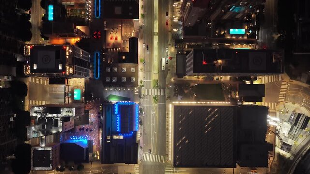 Top down cityscape of downtown Los Angeles at night, showcasing illuminated skyscrapers, bustling streets with vehicle traffic, rooftop pools, modern urban architecture