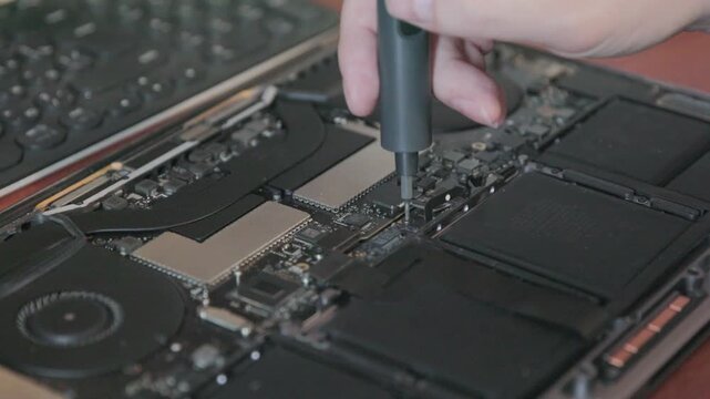 A technician unscrews a screw next to the battery connector inside the laptop case