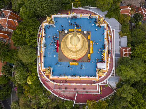 Bangkok, Thailand - 26 April 2026: Aerial view of the golden chedi of Wat Saket Ratchawora Mahawihan with people on the blue platform surrounded by lush greenery and temple roofs.