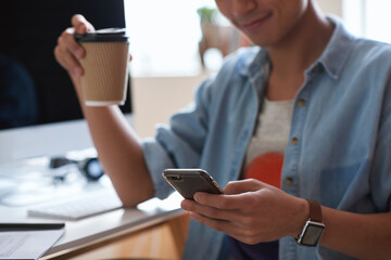 Fototapeta premium Coffee, hands and phone with designer man at desk in office for communication, report or research. App, takeaway drink and typing with design employee at work for chatting, feedback or mobile update