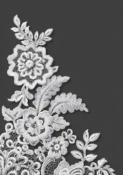 Close-up of delicate white floral lace embroidery, with intricate details of petals and leaves, against a grey background