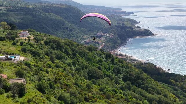 Tracking Aerial View of Paragliding Pacarhute Flying Above the sea and the coastline of Tropea, Italy. Summer Activity and Adrenaline Concept, Drone Shot