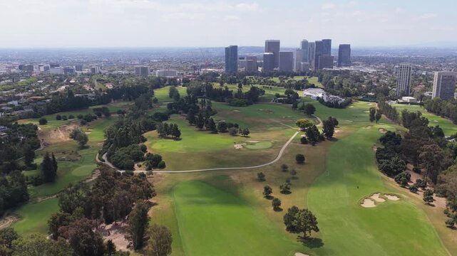 Flying over Los Angeles Country Club towards Century City skyline with golf course greens and fairways in Beverly Hills, California during sunny summer afternoon