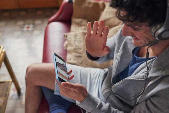 Man, headphones and wave with phone screen for video call, virtual chat or connection with girlfriend. Person, contact partner or online meeting in home with tech, hello or long distance relationship