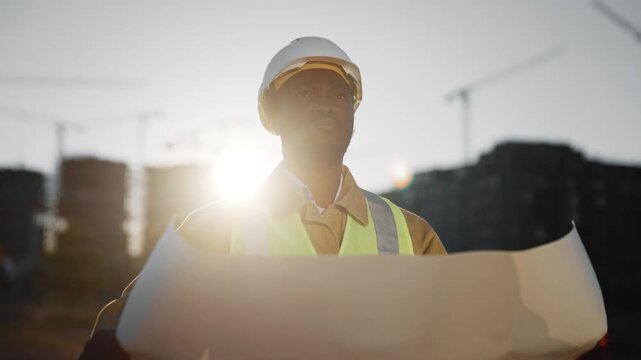 African foreman viewing drawing and inspecting building in construction site. Portrait of professional builder with paper drawing, black male person with hard hat looking up, audit and inspection