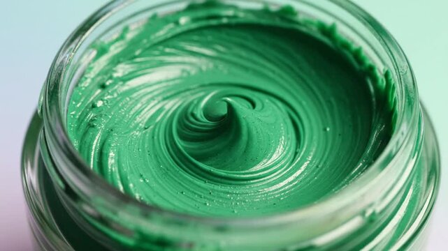 Green organic facial mask cream being swirled in a glass jar close up