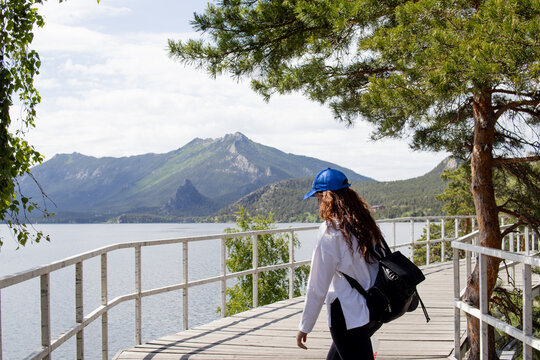 Back view of a young woman admiring the panoramic view of Lake Borovoe, mountains and pine forest in Burabay National Park, Kazakhstan. Travel, nature and outdoor adventure concept.