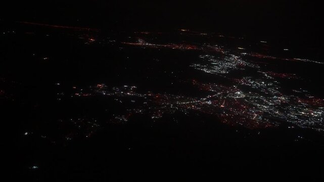 Aerial view of illuminated cityscape at night showcasing vibrant lights and urban layout from an airplane window during flight