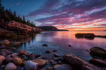 Obraz premium A serene coastal scene at dusk, featuring rocky shorelines, calm water mirroring the colorful sunset and a distant island