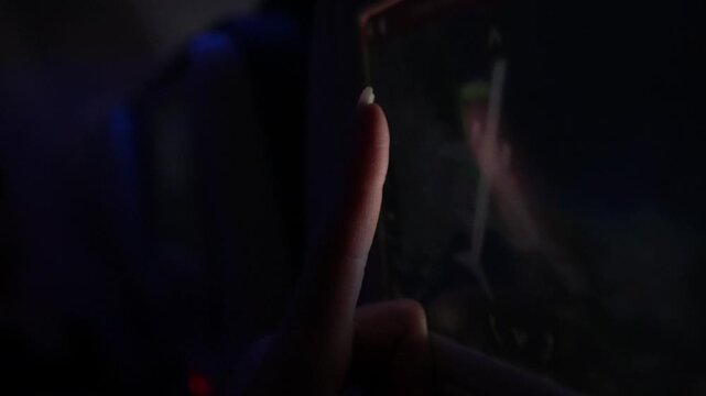 Close-up of hand interacting with touchscreen device, showcasing finger movements and illuminated display in a dimly lit environment