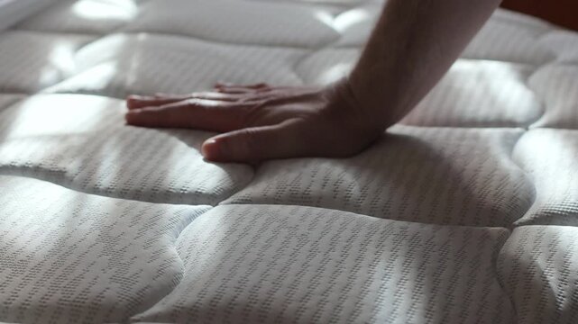 A man presses his hand hard on a new orthopedic mattress, checking the stiffness of the mattress and evaluating its quality before buying in a store, slow motion video
