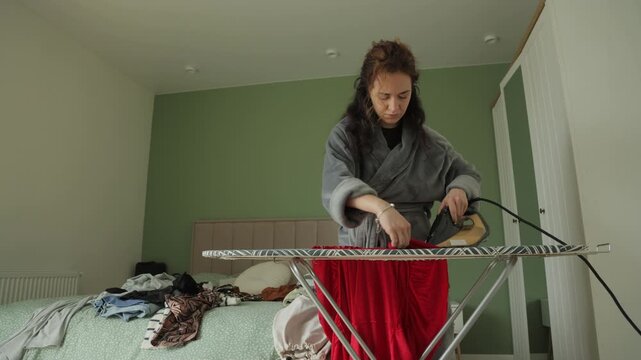 Focused housewife ironing red dress at home