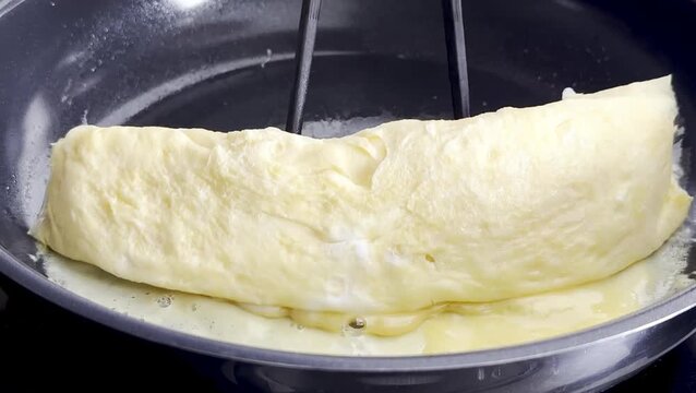 Cooking process of a fluffy omelette being flipped in a non-stick frying pan, showcasing the gradual transformation of the egg mixture into a delicious dish
