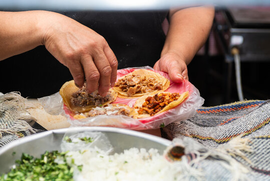 Close-up of hands preparing fresh street tacos with meat, onion and cilantro