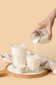 Hand pouring kefir from bottle into glass on beige background