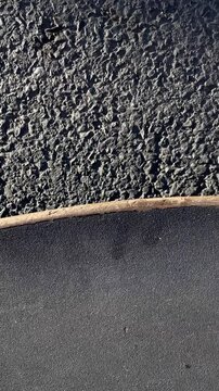 Close deck edge study on rough asphalt, worn grip tape, scuffed nose, shoe sole contact, coarse road texture and tactile street detail