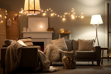 Obraz premium Interior of living room with sofas, fireplace and glowing lights at night