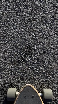Skateboard deck on asphalt pov cruising along smooth pavement sunlight casting crisp shadows sneaker pushing closeup of wheels and grip tape casual