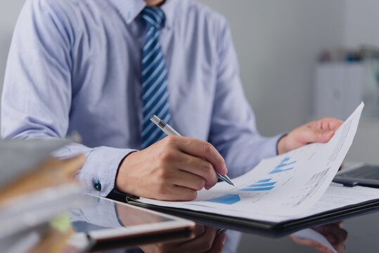 Businessman analyzing financial growth charts holding pen reviewing corporate data reports planning market strategy calculating investment profit on office desk for commercial finance accounting