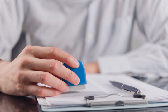Businessman hand pressing rubber stamp on official document verifying contract agreement for corporate compliance certified approval validation visa registration authority commercial use