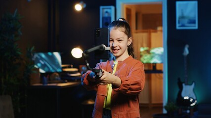 Energetic child dancing and singing, using phone attached to selfie stick to shoot video for social media platforms in living room. Kid entertaining followers, filming with smartphone